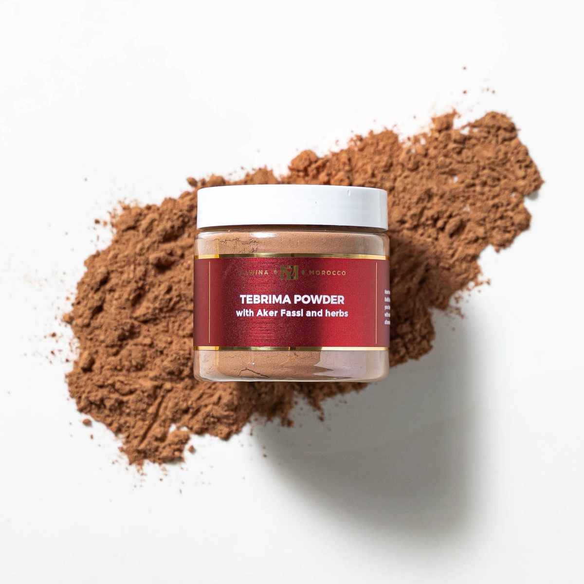 Zawina Morocco Tebrima Powder with Aker Fassi and herbs jar resting over a swatch of fine brown herbal powder